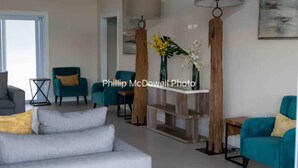 A modern living room with a grey sofa, teal armchairs, and a wooden coffee table. - Ocean Escape - pools, beach, multiple courts, gym (Lucea)