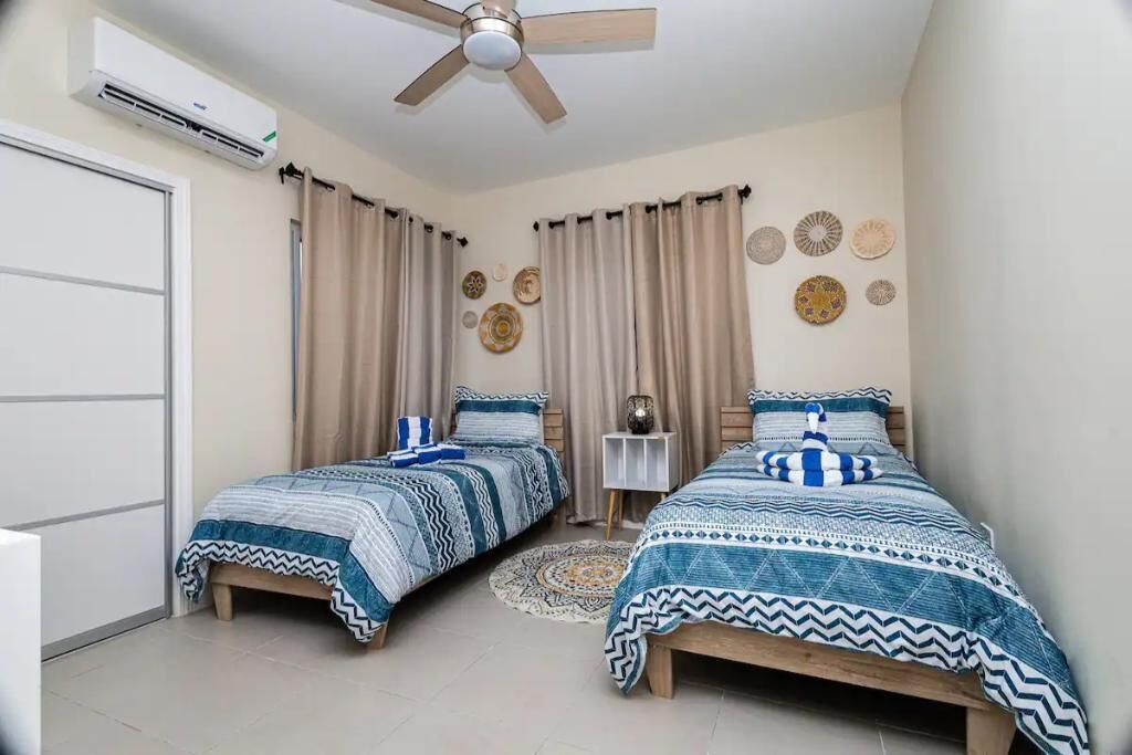 Un dormitorio con dos camas, cortinas color beige, platos decorativos en la pared y un ventilador de techo.