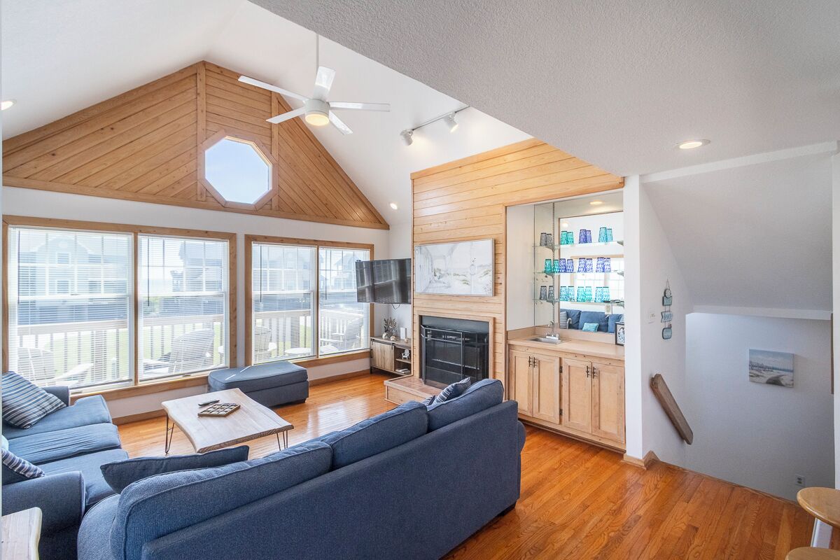 A spacious living area with a high ceiling, wooden beams, a large sofa, a fireplace, and a view of the city.