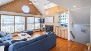A spacious living area with a high ceiling, wooden beams, a large sofa, a fireplace, and a view of the city.