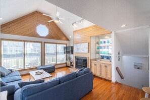 A spacious living area with a high ceiling, wooden beams, a large sofa, a fireplace, and a view of the city. - Beautiful semi-oceanfront townhouse near Kitty Hawk Pier! (Kitty Hawk)