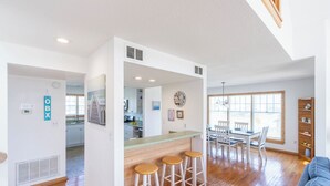 A spacious living area with a wooden floor, a kitchen in the background, and a dining area with a table and chairs.
