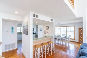 A spacious living area with a wooden floor, a kitchen in the background, and a dining area with a table and chairs. - Beautiful semi-oceanfront townhouse near Kitty Hawk Pier! (Kitty Hawk)