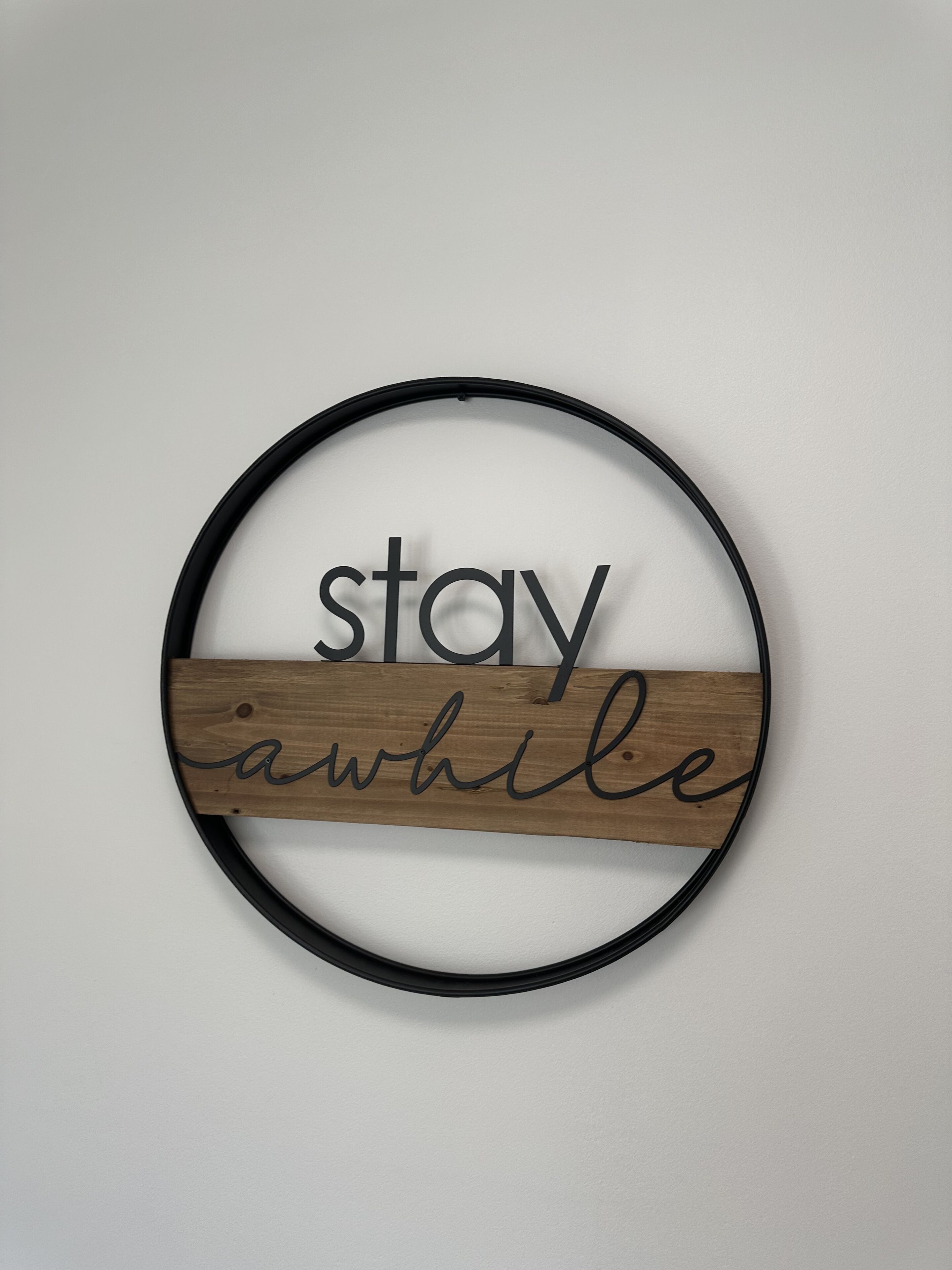 Un élément de décoration murale circulaire, avec l’inscription « restez un peu » dans un cadre en bois.