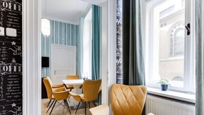 A modern dining area with a white table and four chairs, a large window with curtains, and a wall with coffee-related text. - Beautiful Apartment in Prague (Prague)