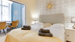 A hotel room with a large bed, two bedside lamps, a window with curtains, a desk with a chair, and a patterned wallpaper. - Beautiful Apartment in Prague (Prague)