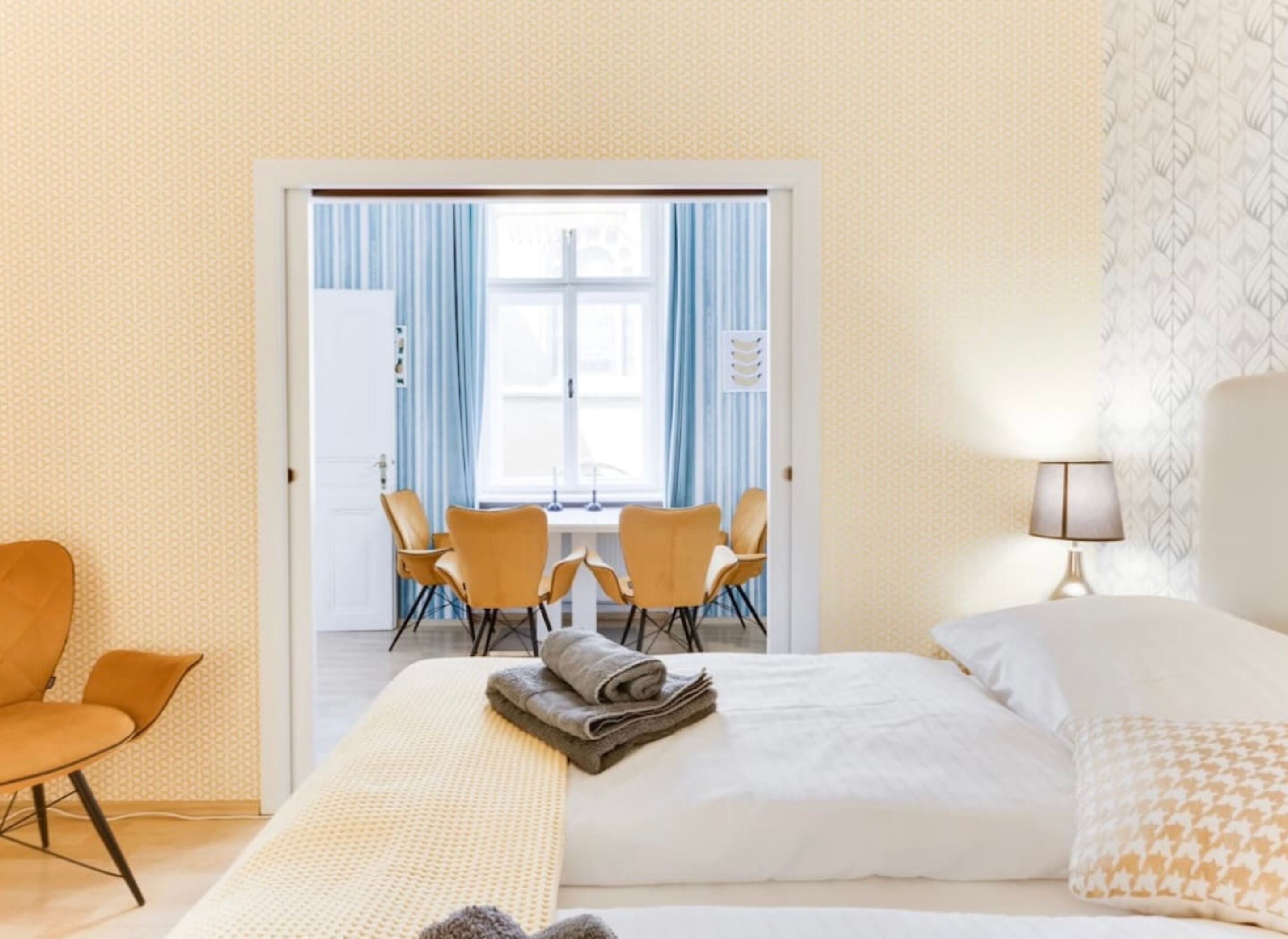 Habitación de hotel con una cama, una silla, una mesa con sillas y vistas a través de una puerta.