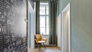 A hallway with a wall covered in coffee-related drawings and text, a window with curtains, and a chair in the center. - Beautiful Apartment in Prague (Prague)