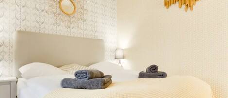 A neatly made bed with two rolled towels, a bedside lamp, and a wall-mounted mirror.