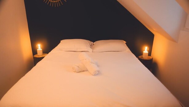 A neatly made bed with white linens and a rolled towel, two bedside lamps, and a dark ceiling. - Le Racine, Charmant T3 en Centre Ville (Tours)