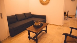 A living room with a dark-colored sofa, a wooden coffee table with a woven basket, and a wall-mounted circular mirror. - Le Racine, Charmant T3 en Centre Ville (Tours)