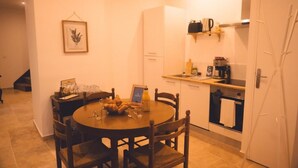A compact kitchen with a dining table and chairs, a refrigerator, a coffee machine, and a small oven. - Le Racine, Charmant T3 en Centre Ville (Tours)