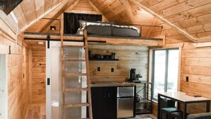 A compact wooden cabin with a loft bed, kitchenette, and a dining area.