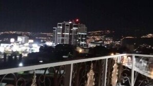 Une vue nocturne sur le paysage urbain, prise depuis un balcon orné de balustrades en métal ouvragé.
