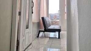 Un couloir avec un banc en cuir noir, un sol carrelé en pierre et une vue sur l’extérieur par une fenêtre.