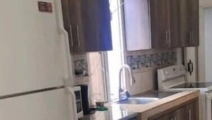 Eine Küche mit dunklen Holzausziehtüren, einem weißen Kühlschrank, einer Spüle und einem Fenster mit Vorhängen.
