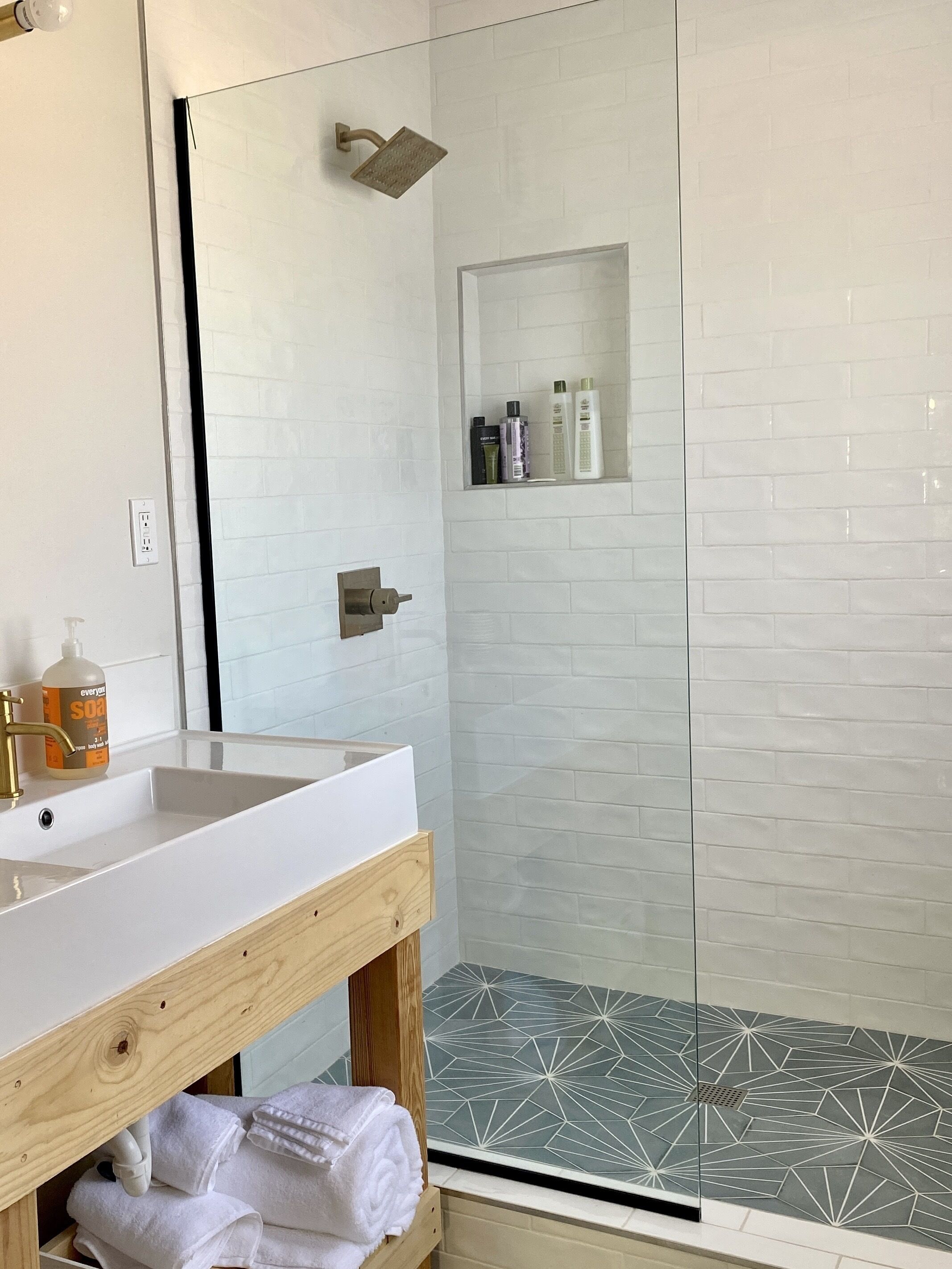 A bathroom with a white sink, wooden vanity, a glass shower enclosure, and a tiled shower floor.
