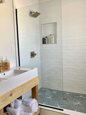 A bathroom with a white sink, wooden vanity, a glass shower enclosure, and a tiled shower floor.