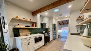 A modern kitchen with white cabinets, a stainless steel refrigerator, a built-in oven, and a large island with a sink. - Joshua Tree- Hot tub, Walk to food & shops, a few minutes from JTNP (Joshua Tree)