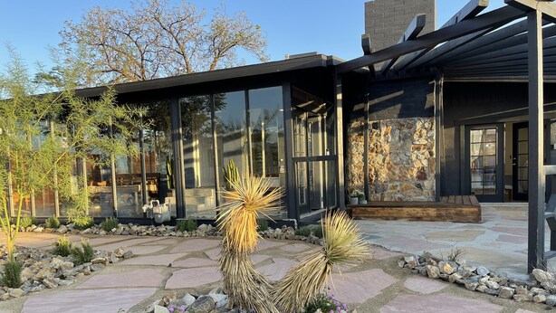 A modern building with a stone facade, large windows, and a patio area with rocks and cacti. - Joshua Tree- Hot tub, Walk to food & shops, a few minutes from JTNP (Joshua Tree)