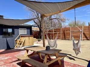 A wooden picnic table with benches, a hanging hammock, and a shaded area with a wooden pergola.