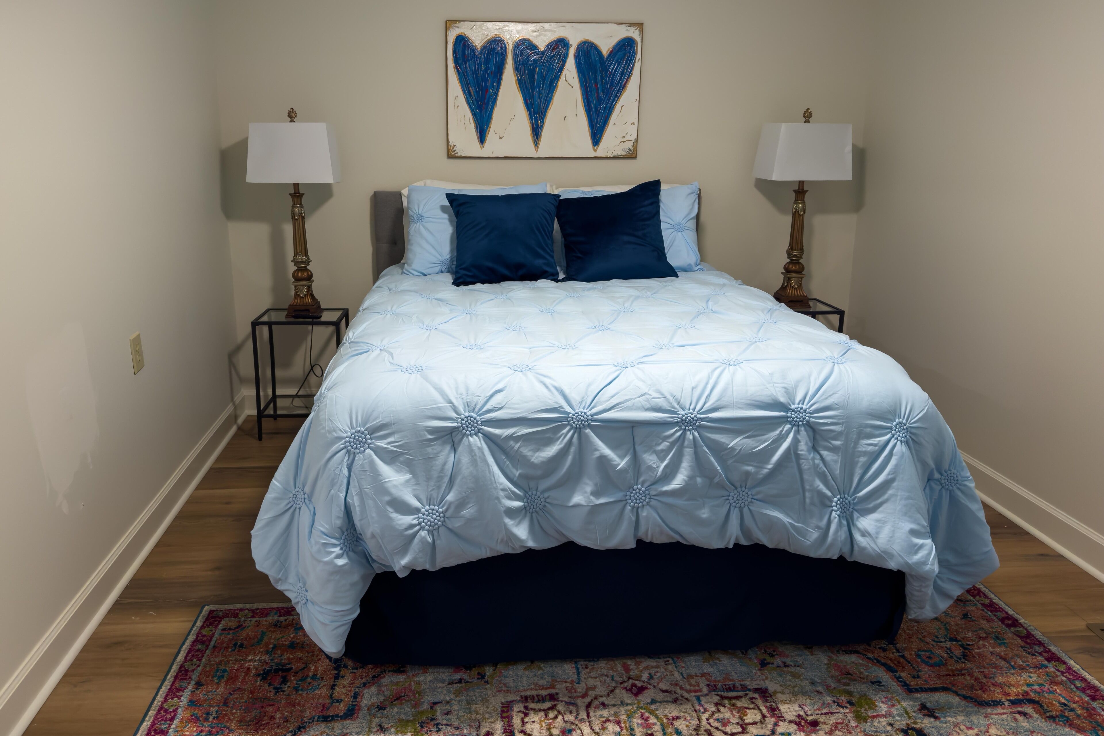 Un dormitorio con una cama grande, dos lámparas de noche, un tapete estampado y una obra de arte en la pared.