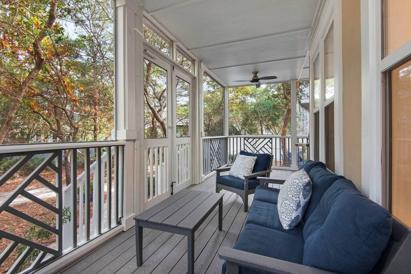 A covered porch with a wooden deck, a dark blue sofa with patterned cushions, and a ceiling fan.