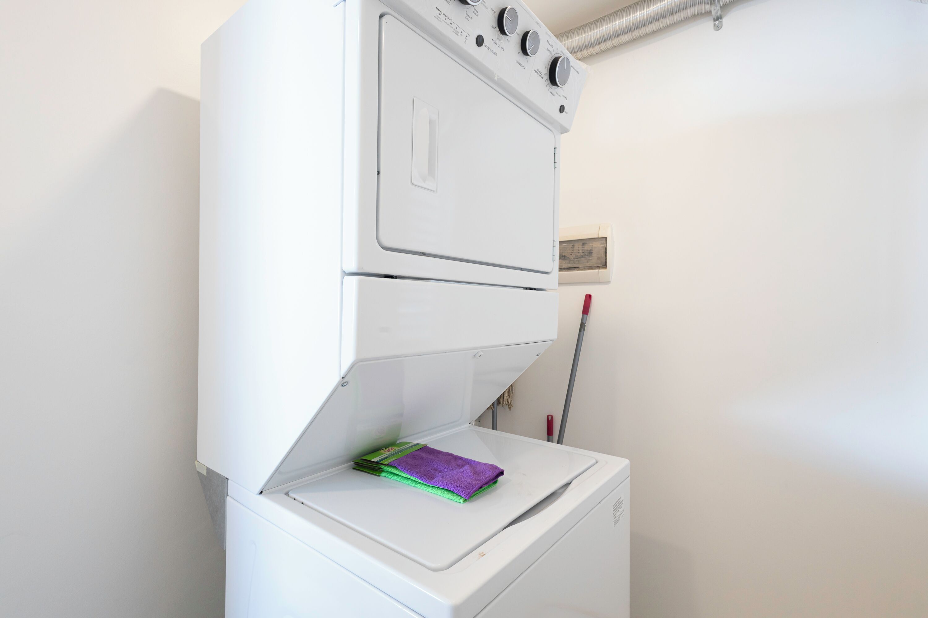 A white stacked washer and dryer unit with a purple towel on the lower unit.