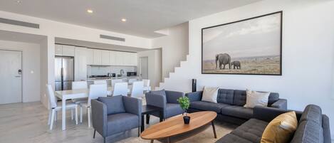 Una sala moderna con un sofá gris, una mesa de centro de madera y un comedor con sillas blancas.