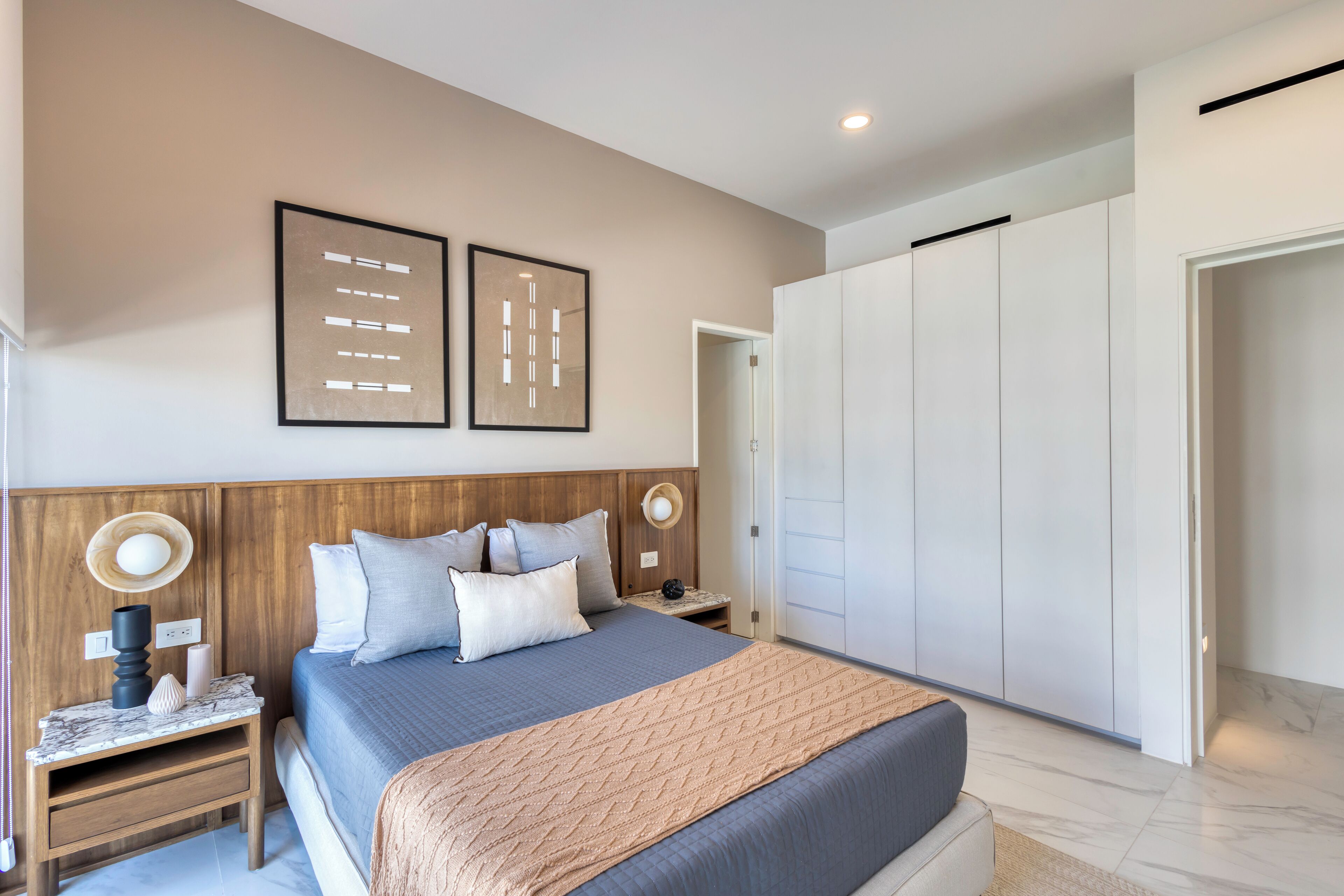 Een moderne slaapkamer met een groot bed, een houten hoofdbord, nachtkastjes met lampen en een kledingkast.