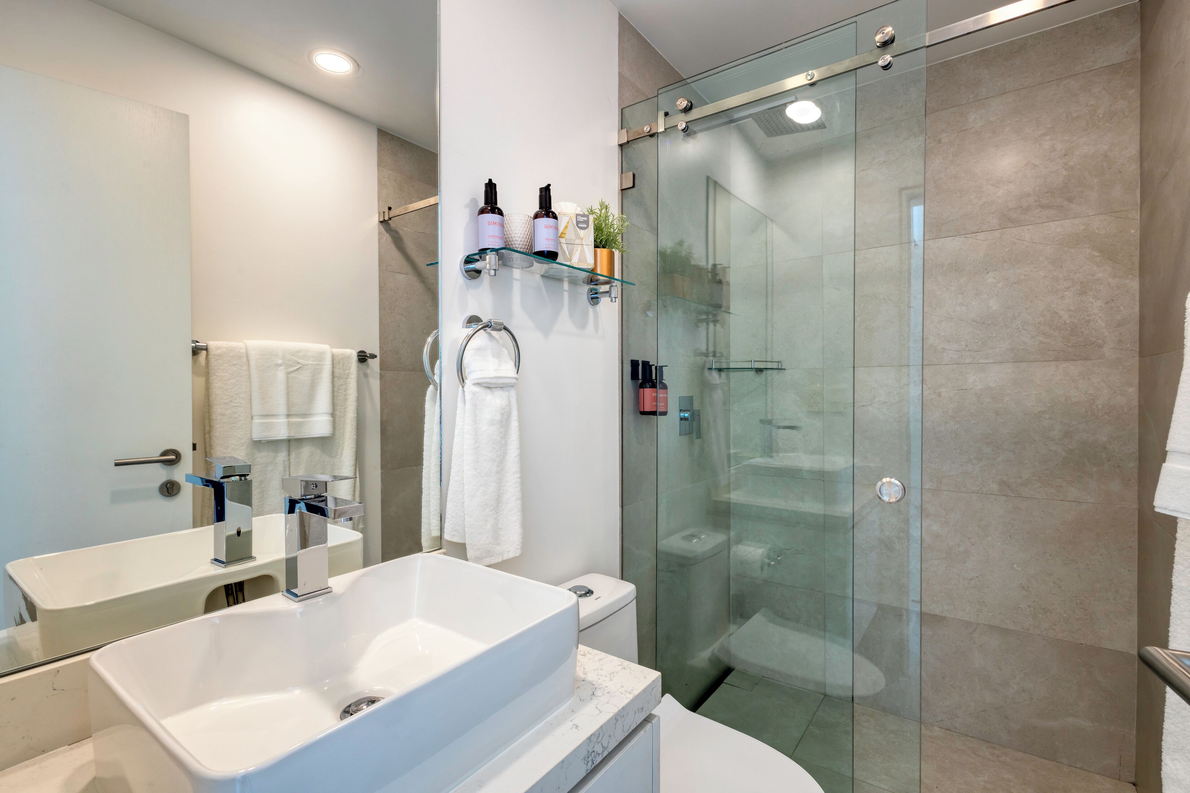 Un baño moderno con ducha de vidrio, un lavamanos grande de color blanco y un espejo.