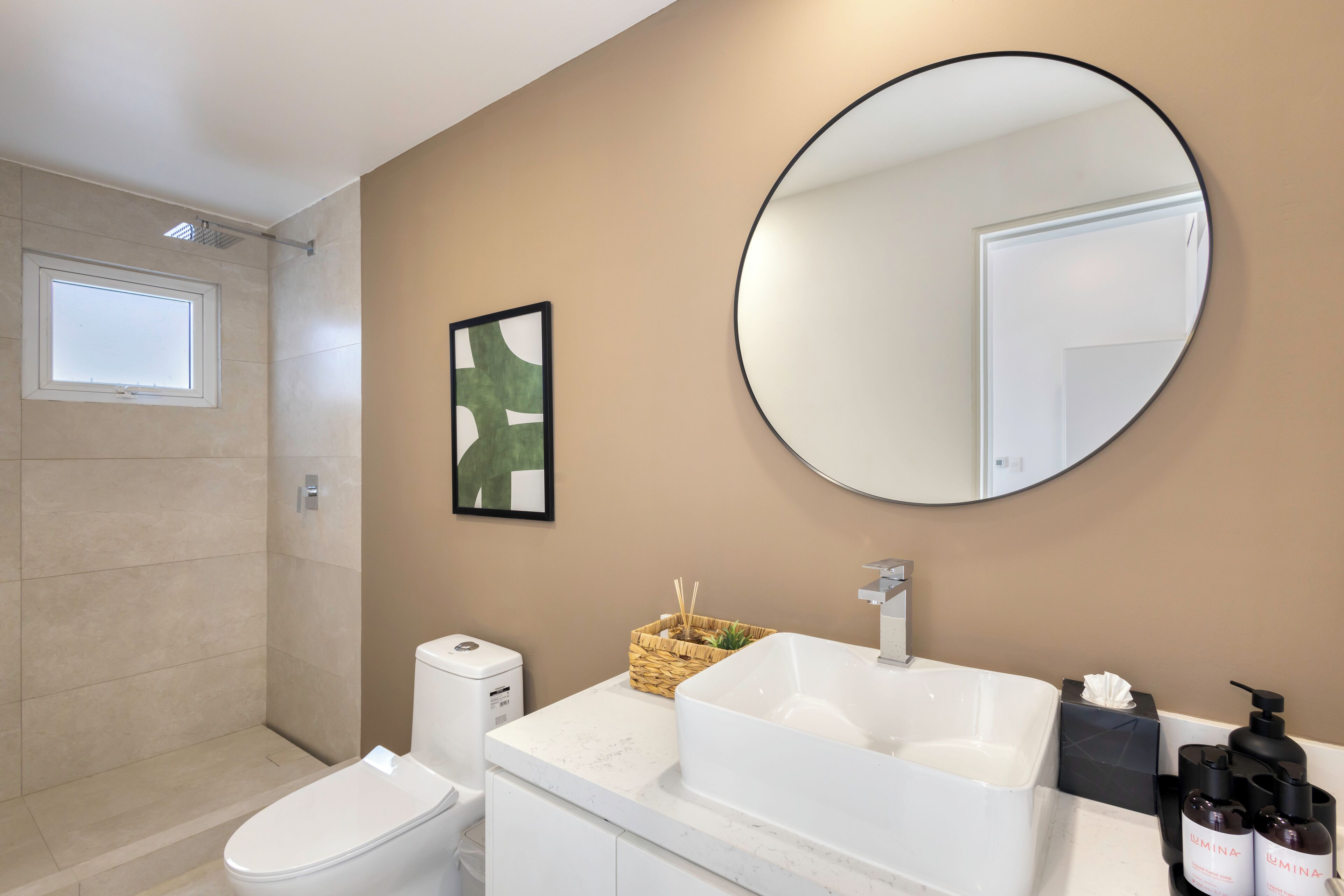Une salle de bain moderne avec un grand miroir rond, un lavabo blanc et des toilettes.