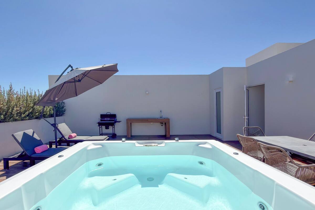 Una terraza en la azotea con un jacuzzi, sillones de descanso, una mesa y una parrilla.