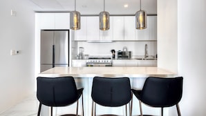 A modern kitchen with a central island, black chairs, stainless steel appliances, and pendant lighting.