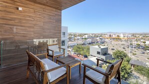 A balcony with wooden flooring and furniture, overlooking a cityscape with buildings and a parking lot.