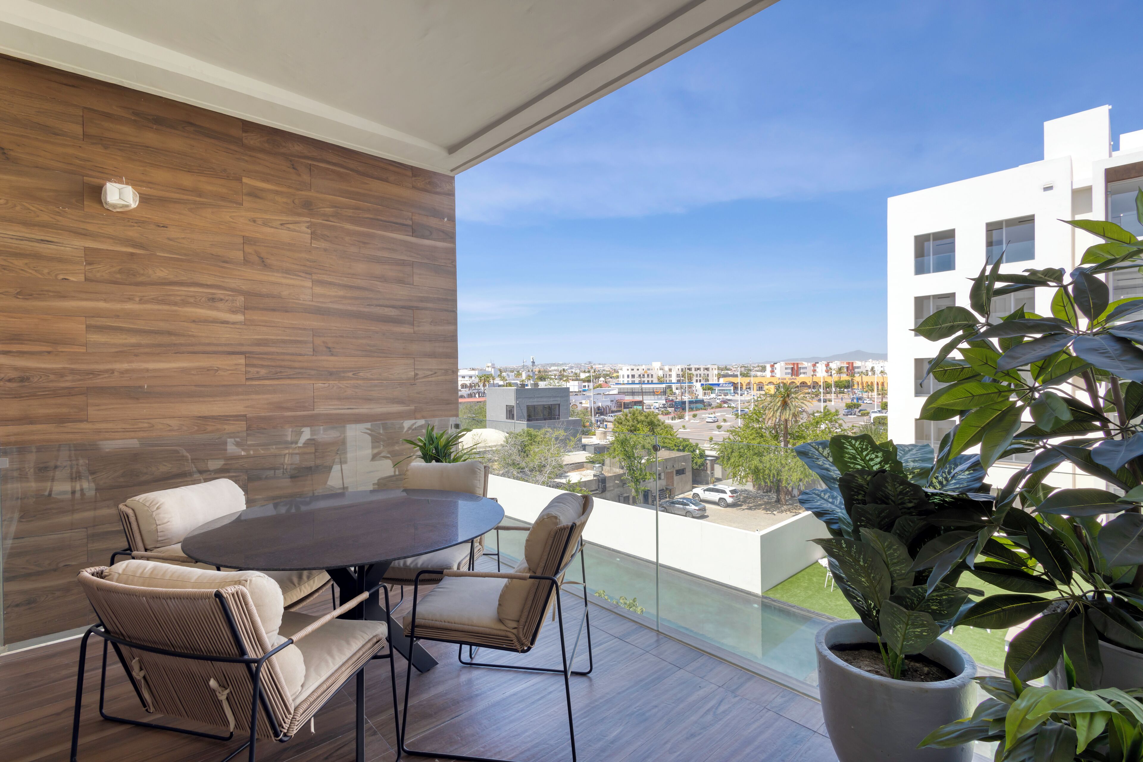 Un balcon doté d’un plancher en bois, d’une table ronde et de chaises, offrant une vue sur le paysage urbain.