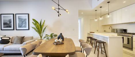 Una cocina moderna con armarios blancos, una isla central y una zona de comedor con mesa y sillas de madera.