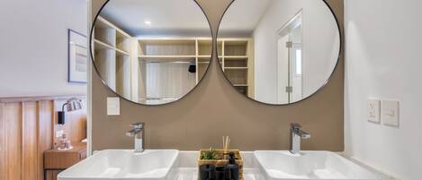 A bathroom with two sinks, a mirror, and a vanity with a plant and toiletries.