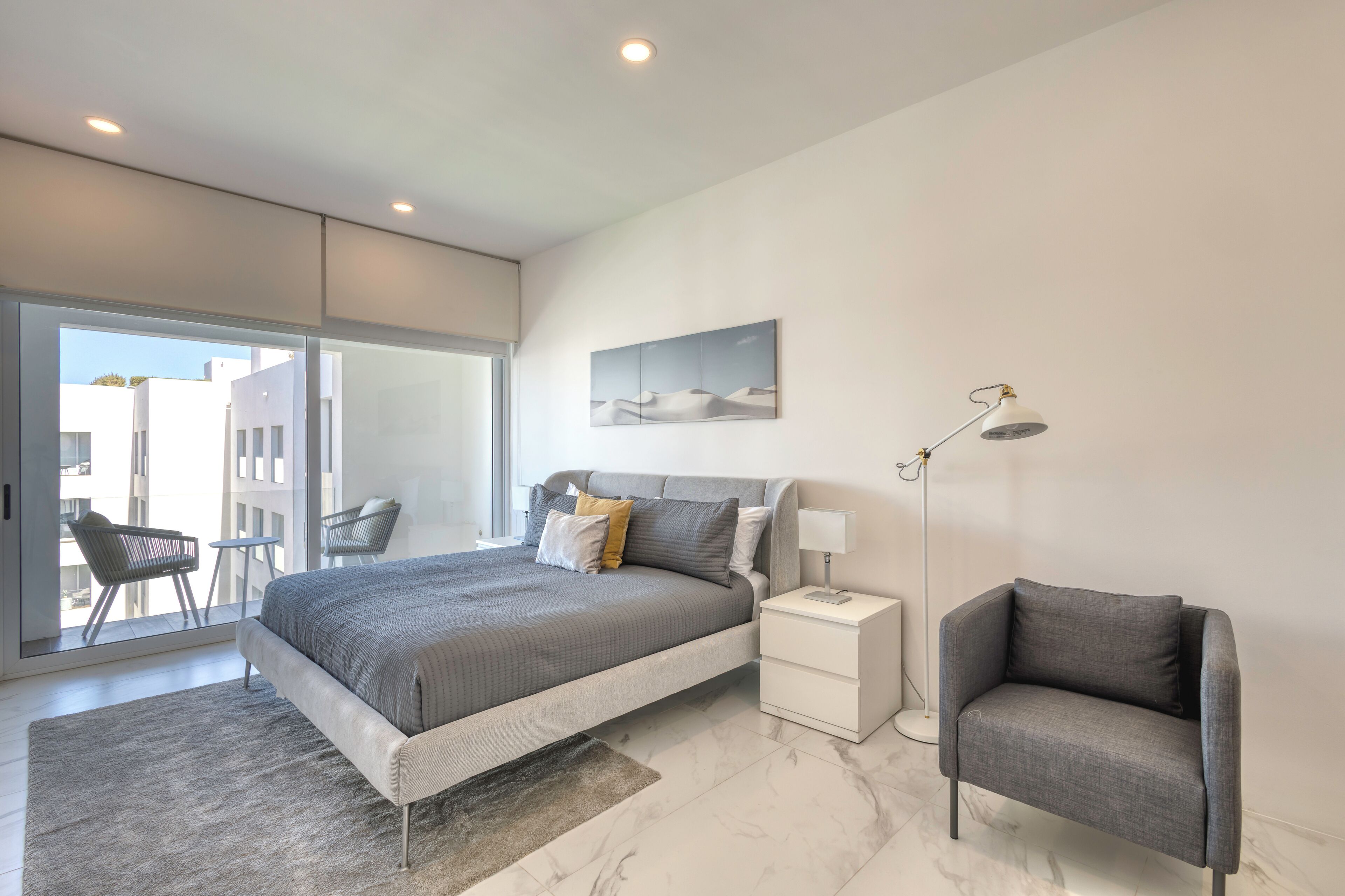 A modern bedroom with a large bed, a nightstand, a chair, and a floor lamp.