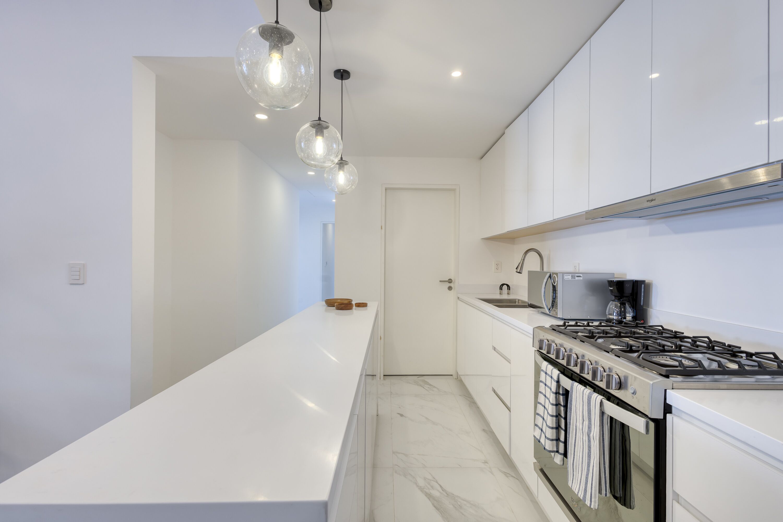 A modern kitchen with white cabinetry, a central island, a gas stove, and pendant lighting.