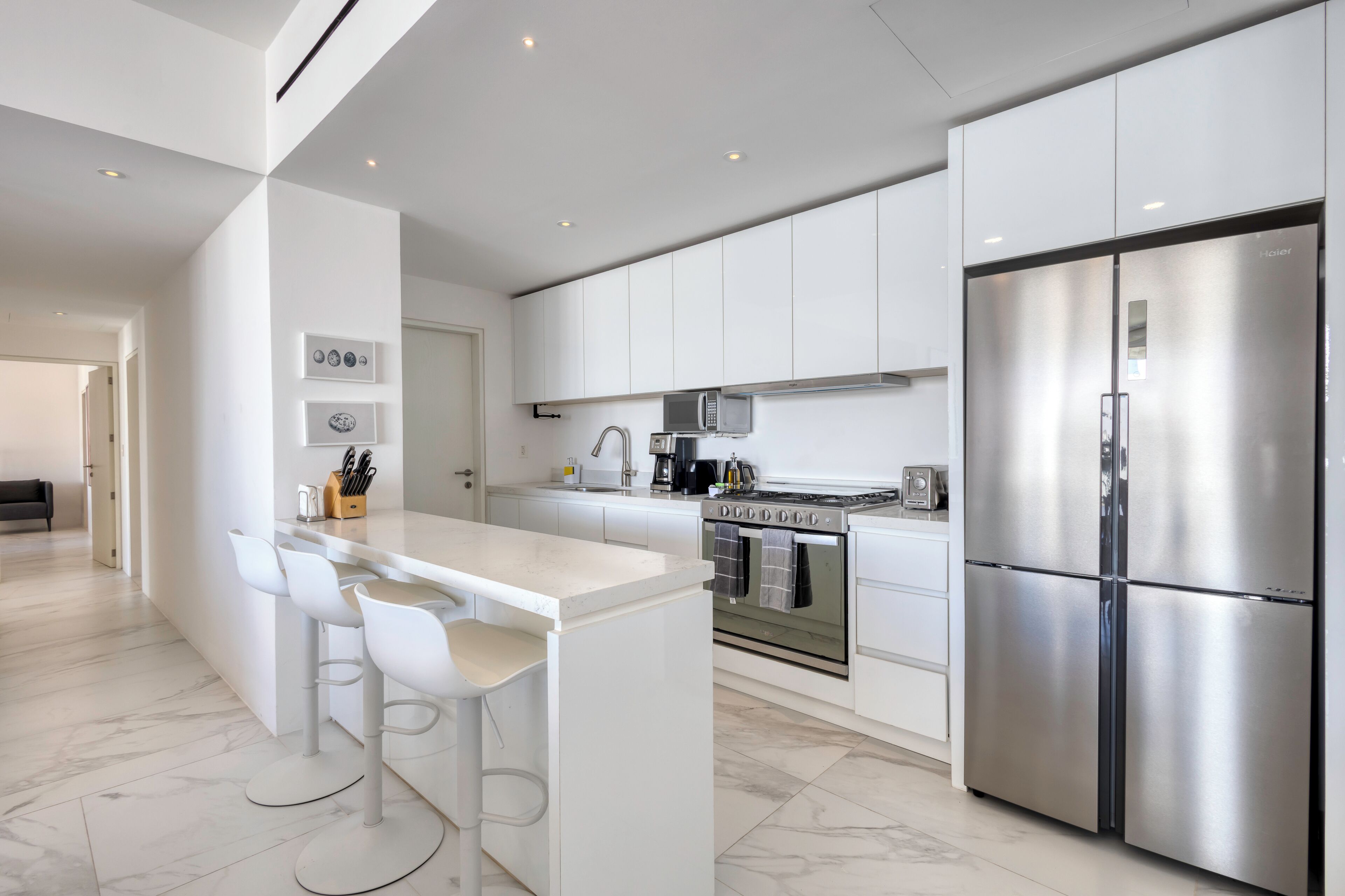 A modern kitchen with white cabinetry, a stainless steel refrigerator, and a central island with bar stools.