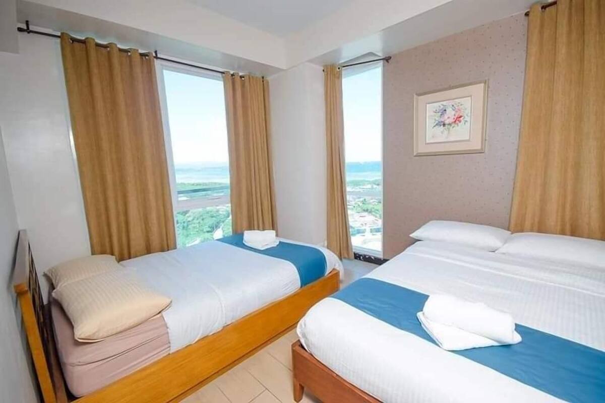 A hotel room with two beds, beige curtains, a framed picture on the wall, and a view of the landscape.