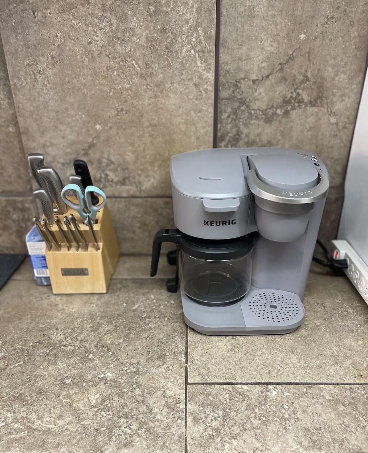 A Keurig coffee maker on a tiled floor next to a knife block.