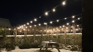 A stone wall with string lights above, a bench, and snow on the ground. - The Shearer's Hut (Holmfirth)