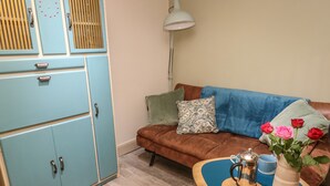A cozy living room with a brown sofa, a blue cabinet, a small table with a vase of flowers, and a floor lamp. - The Shearer's Hut (Holmfirth)