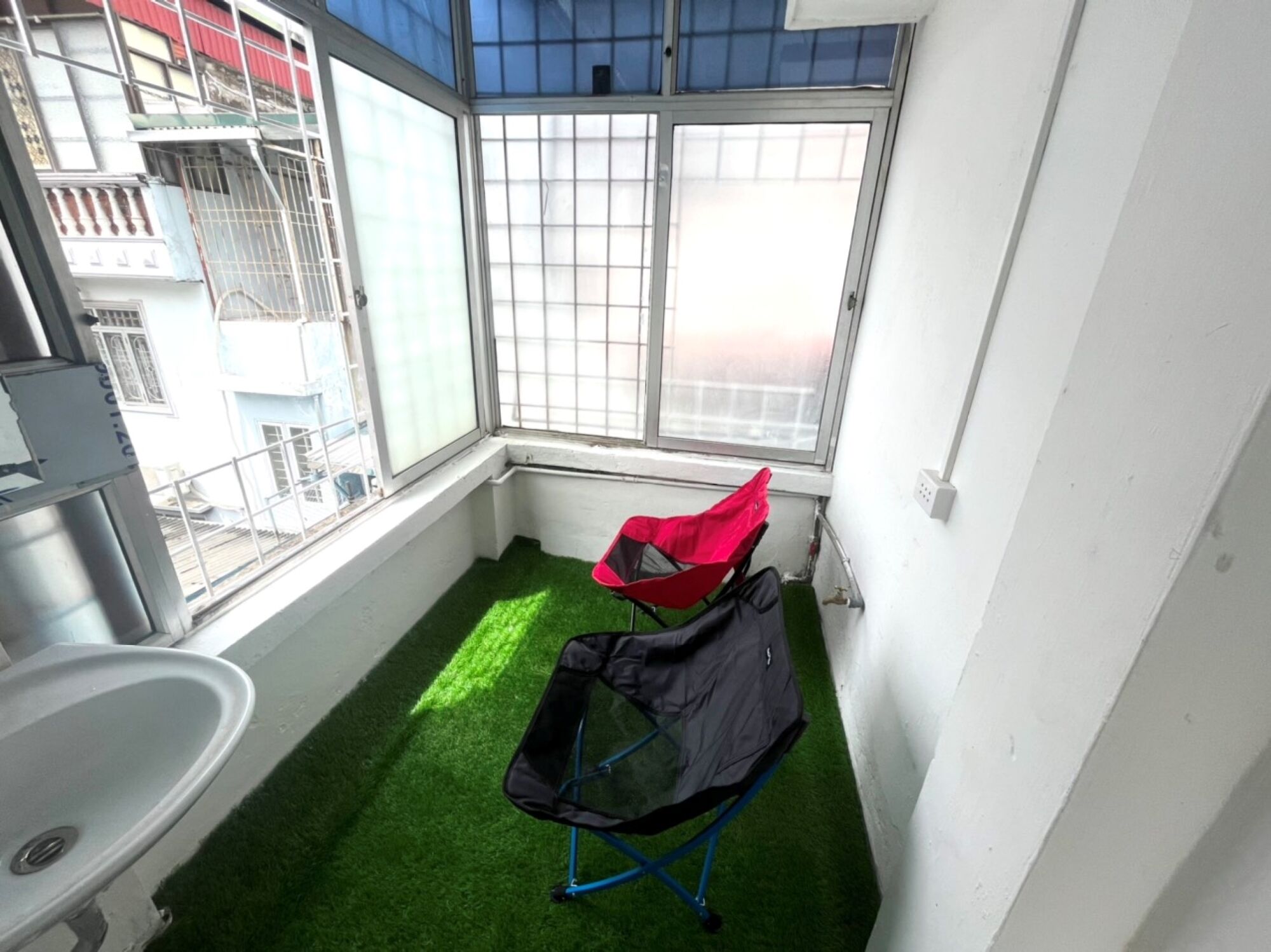A small balcony with artificial green turf, a red and black folding chair, and a white sink.
