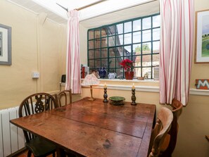 A wooden dining table with chairs, a window with a view of greenery, and a potted plant on the windowsill. - Yew Tree Cottage (Leominster)