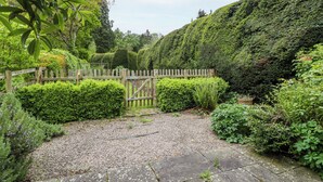 Un jardín con una verja de madera, un sendero de grava y diversos arbustos verdes.