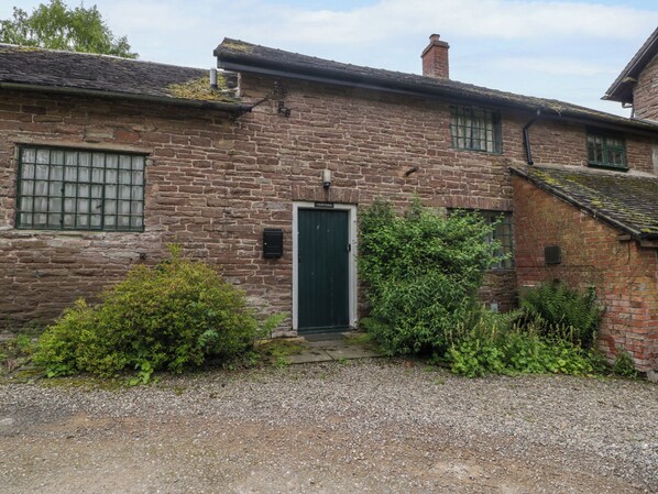 A traditional stone building with a green door, a small window with bars, and a gravel driveway. - Yew Tree Cottage (Leominster)