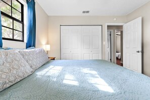 Une chambre à coucher avec un lit, une fenêtre avec des rideaux, une armoire et une porte donnant sur une autre pièce.